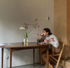 a woman sitting at a wooden table eating food and drinking milk from a glass vase