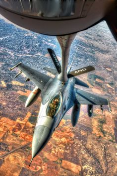 a fighter jet flying through the sky over land and water in front of an airplane