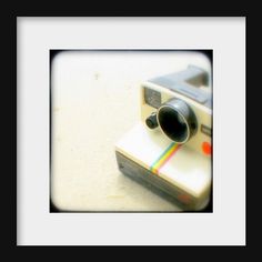 a polaroid camera sitting on top of a white table next to a black frame