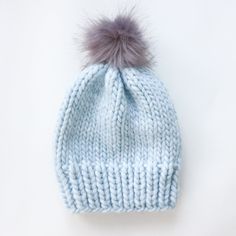 a light blue knitted hat with a grey pom - pom on top