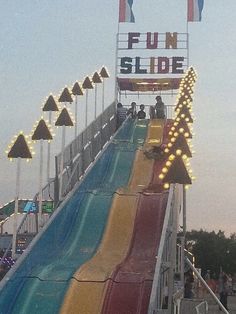 people are riding down the slide at an amusement park with lights on it's sides