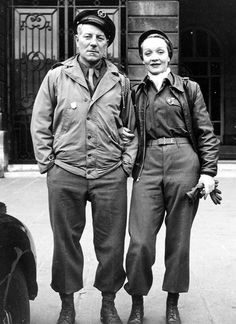 an old black and white photo of two people standing next to each other in front of a building