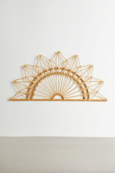 a wall sculpture made out of gold wire on a white wall with a plant in the corner