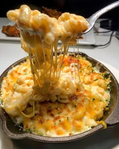 a fork lifting up some macaroni and cheese from a skillet on a table