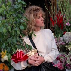 a woman standing in front of flowers holding a purse