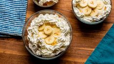 three bowls filled with bananas and whipped cream on top of a wooden table next to a blue towel