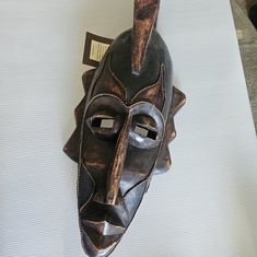 a wooden mask hanging on the wall with a tag attached to it's side