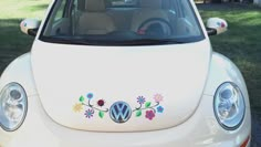 a white volkswagen car with flowers painted on the front and side windows, parked in a driveway