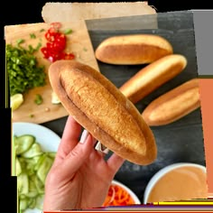 a person holding up a sandwich in front of some vegetables and breadsticks on a cutting board