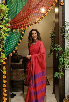 a woman in a red and purple sari standing at the entrance to her home