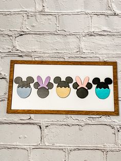 mickey and minnie mouse ears cut outs on a white brick wall above a wooden frame