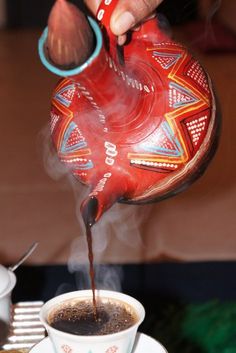 a person pouring coffee into a cup on top of a saucer with steam coming out of it