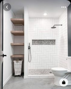 a white toilet sitting in a bathroom next to a walk in shower and wooden shelves