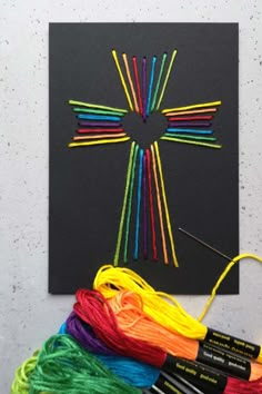 a cross made out of colored yarn next to some crochet hooks and thread