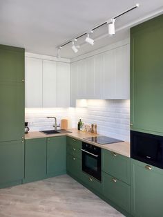 an empty kitchen with green cabinets and white tile backsplash, lights above the sink