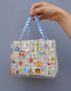 a hand is holding a purse with many charms on it and hanging from the handle