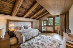 a bedroom with a large bed and wooden ceiling, along with a white fur rug on the floor