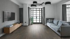 a living room with wood flooring and gray couches in front of a flat screen tv mounted on the wall