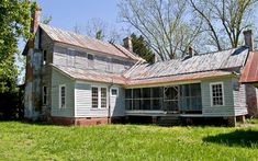 an old run down house sitting in the middle of a field with grass and trees