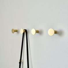 three brass knobs and two black leather straps hang on a white wall in an otherwise empty room