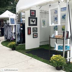 a white tent with paintings and pictures on the wall next to flowers in potted planters