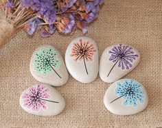 four painted rocks with dandelions on them sitting next to some purple and white flowers