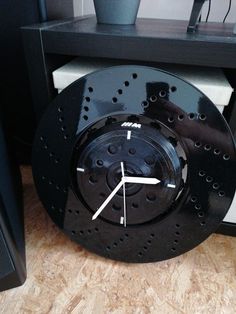 a clock that is sitting on the floor next to a shelf with a plant in it