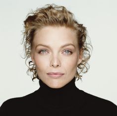 a woman with curly hair wearing a black turtle neck sweater and posing for the camera