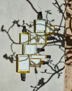 four bottles of perfume sitting on top of each other next to a shadow of a tree