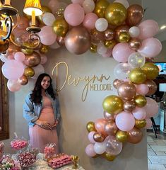 a pregnant woman standing in front of a display of balloons and desserts at a baby shower