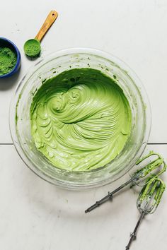 a bowl filled with green liquid next to two whisks