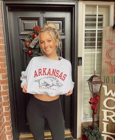 a woman standing in front of a door wearing a gray sweatshirt and black leggings