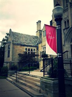 a red and white flag hanging from a light post in front of a large building