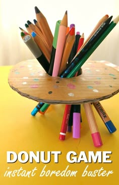 a wooden holder filled with colored pencils on top of a yellow table next to the words donut game instant boredom buster