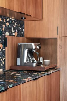 a coffee maker is sitting on the counter in a kitchen with wood cabinets and black wallpaper