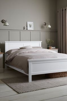 a white bed sitting in a bedroom on top of a wooden floor next to a window