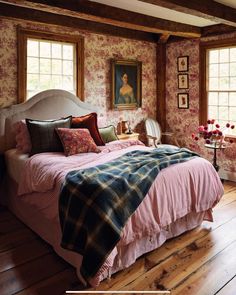 a bed sitting in a bedroom next to two windows with paintings on the wall behind it