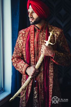 a man in a red turban is holding a golden object and looking out the window