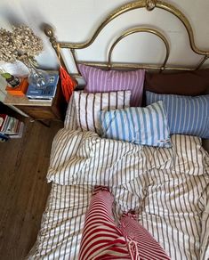 an unmade bed with striped sheets and pillows on top of it, next to a night stand