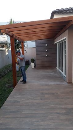 a man standing under a wooden pergolan on top of a patio next to a house