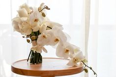 a bouquet of white flowers sitting on top of a wooden table next to a window