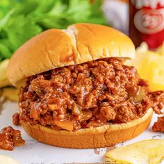 a sloppy joe sandwich sitting on top of a table next to chips and ketchup