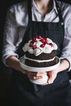 a person holding a cake with white frosting and raspberries on the top