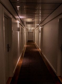 an empty hallway with lights on the ceiling and carpeted floor, leading to another room