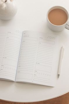 an open notebook sitting on top of a white table next to a cup of coffee