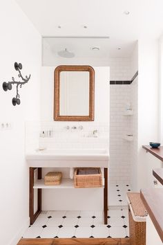 a white bathroom with black and white tile flooring, wooden framed mirror above the sink