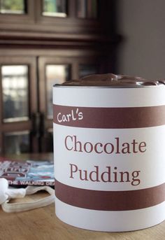 a can of chocolate pudding sitting on top of a wooden table next to a book