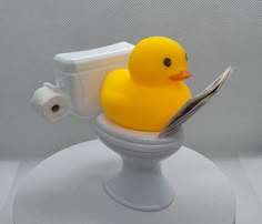 a yellow rubber ducky sitting on top of a toilet seat reading a paper towel