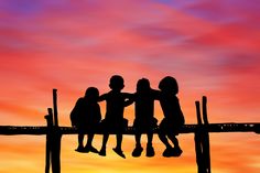 three children are sitting on a wooden dock as the sun sets in the sky behind them