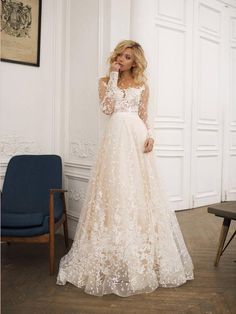 a woman in a wedding dress standing next to a chair and looking at the camera